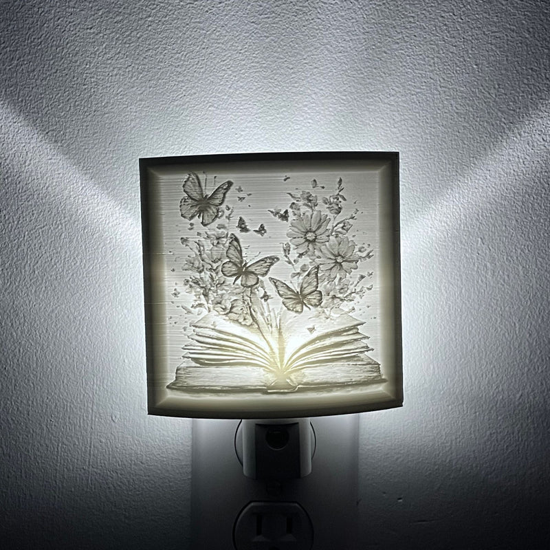 nightlight with a depicting an open book with flowers and butterflies emerging from it.