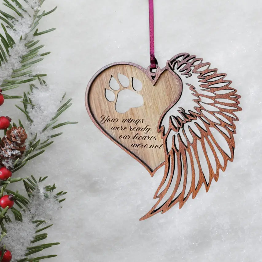 Handmade wooden dog memorial ornament with paw print and angel wing hanging on holiday greenery, personalized pet remembrance gift.
