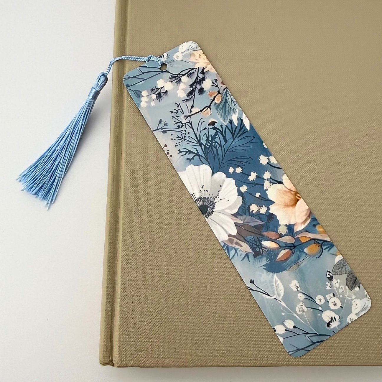 Blue floral bookmark resting on a beige book with a light blue tassel.