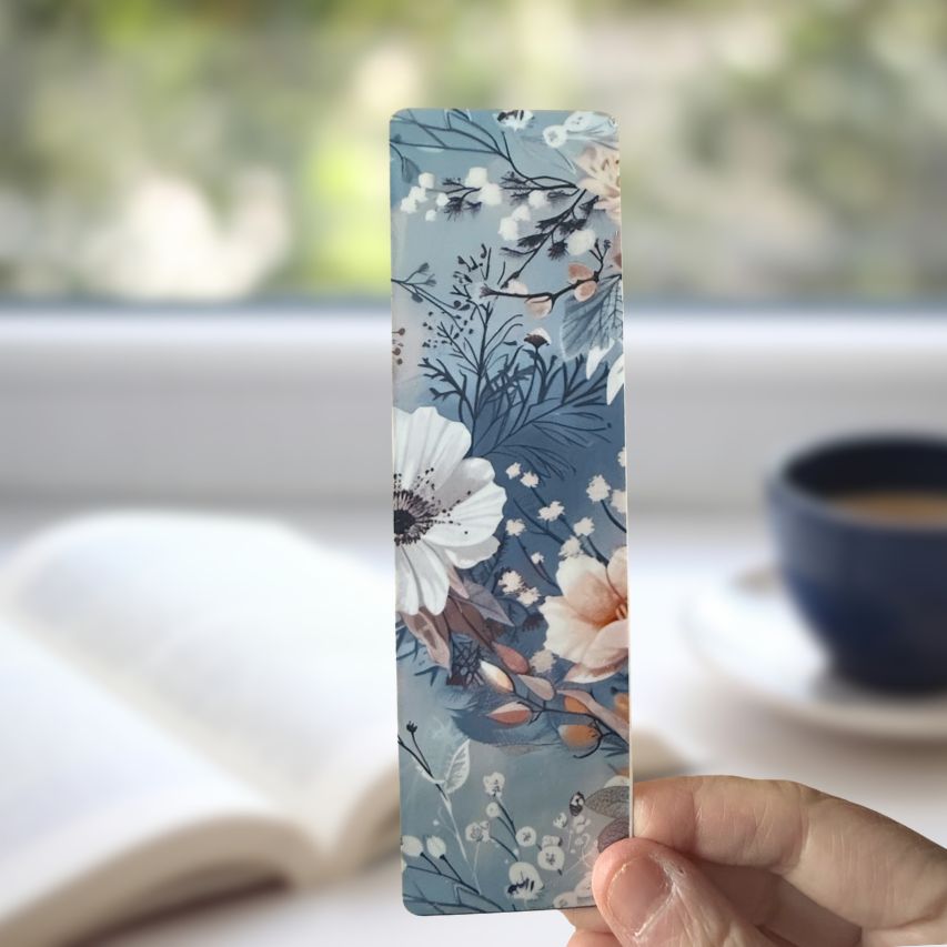 Floral bookmark held by a hand with a blurred background of a book and cup.