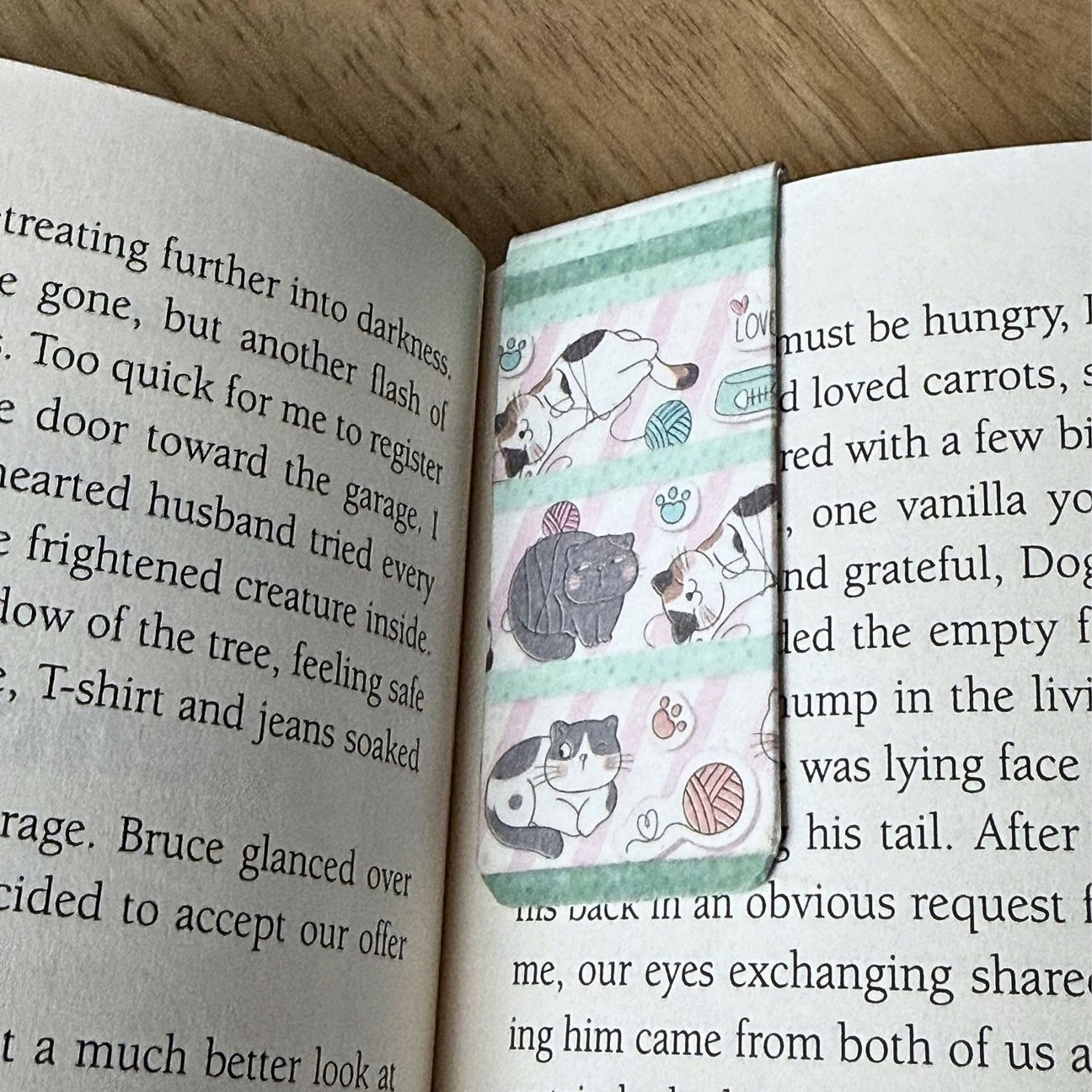 Open book with a bookmark featuring cat illustrations on a wooden surface