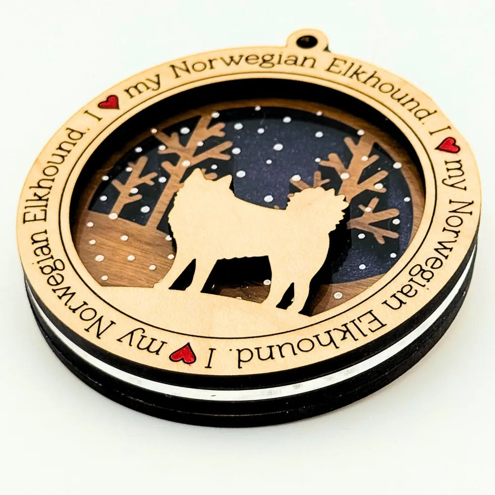 Decorative wooden ornament with a silhouette of a Norwegian Elkhound with a dark blue background and engraved text on a white background.