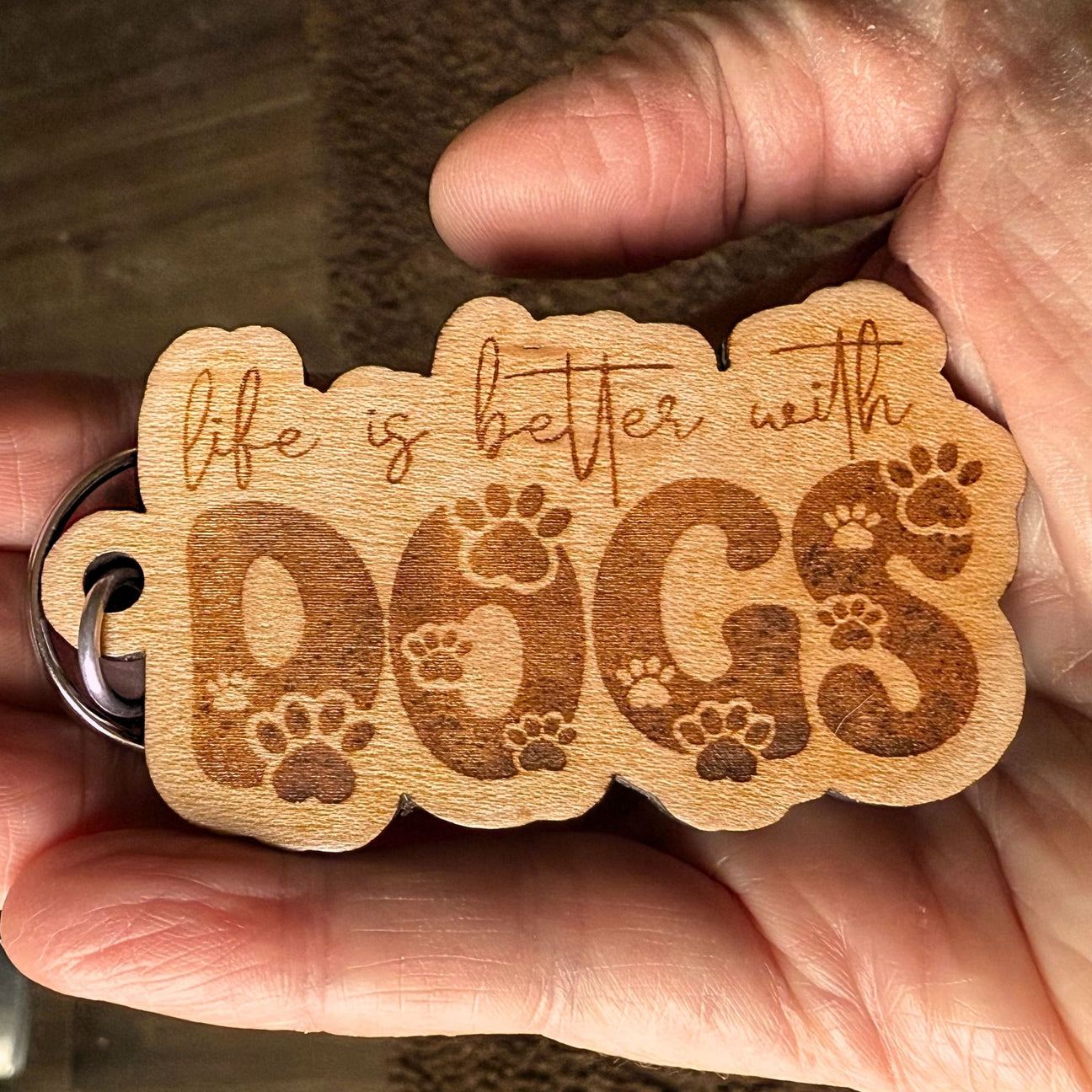 Wooden keychain with 'life is better with dogs' text held in a hand.