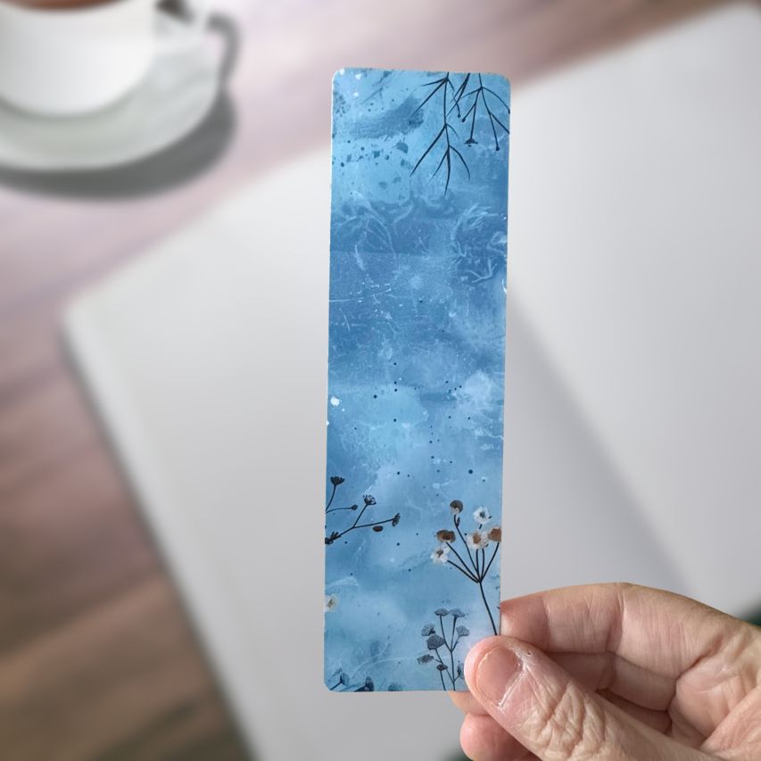Hand holding a blue floral bookmark with a blurred background