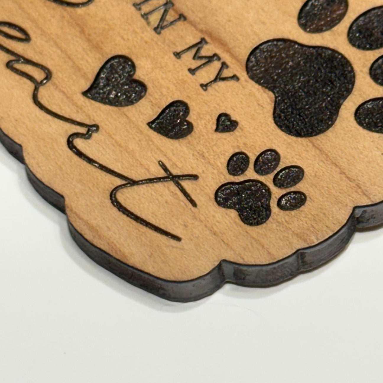 Close up view of a wooden keychain with paw prints and text on a white background