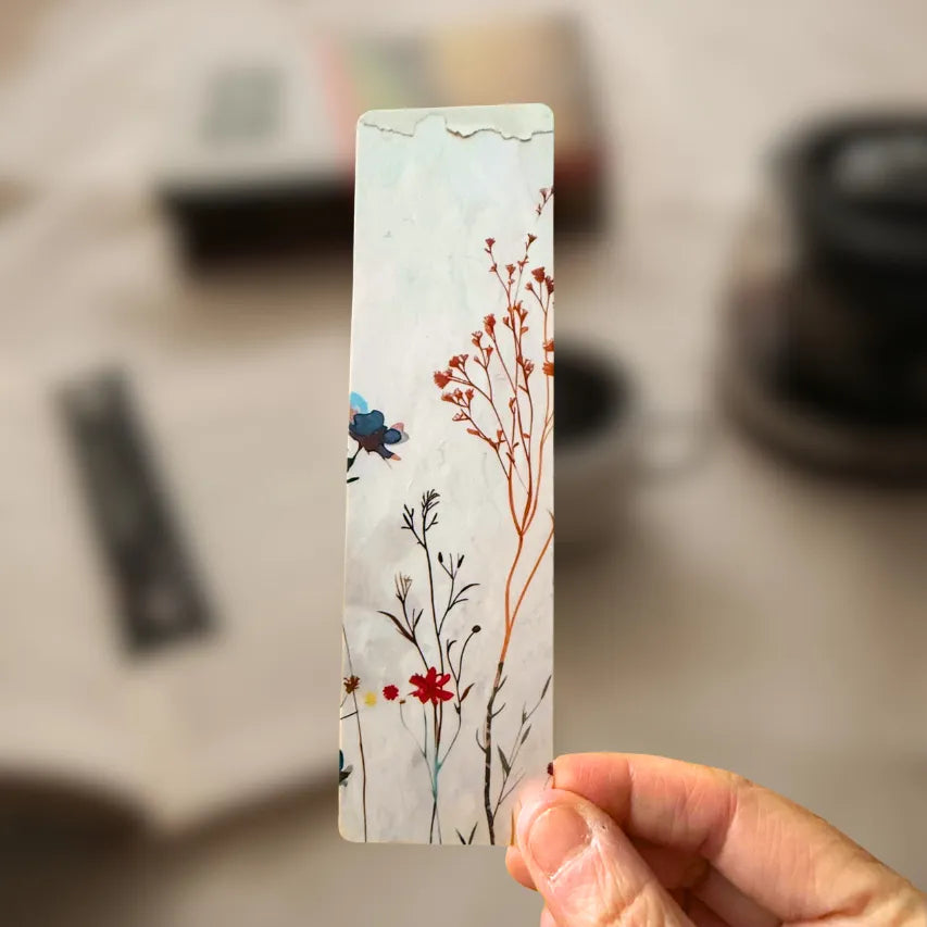 Tan floral bookmark held in hand over a blurred background.