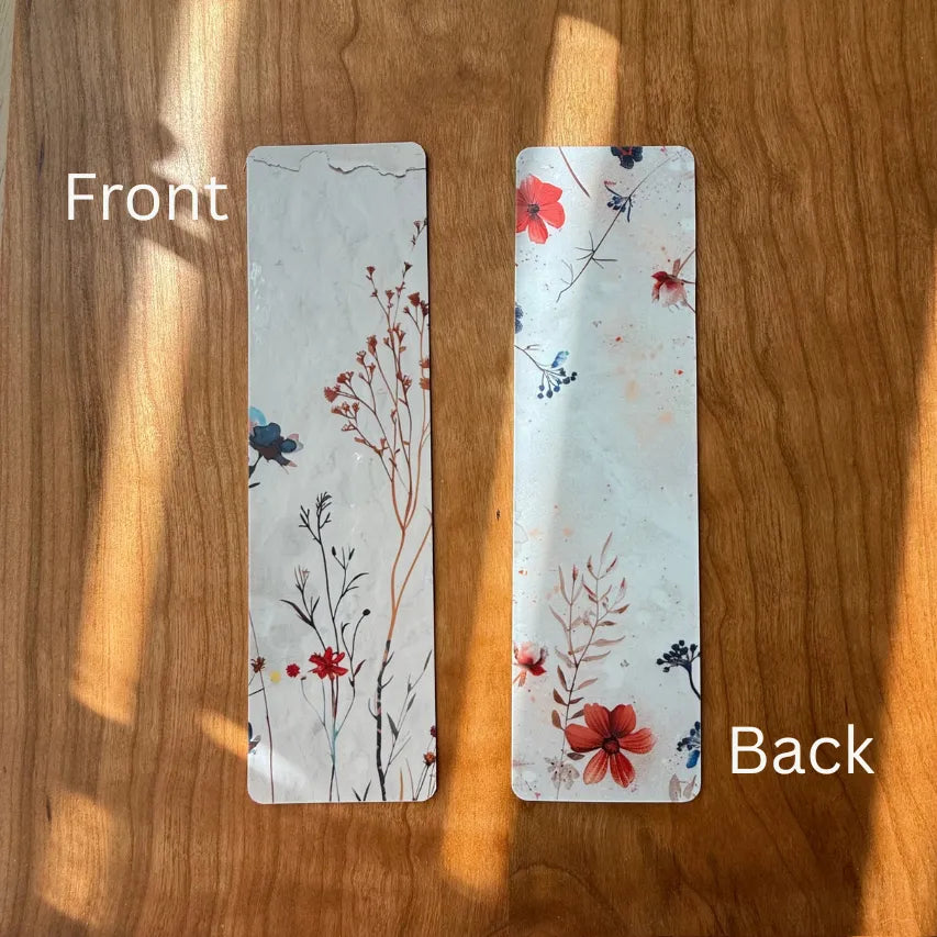 Tan floral bookmark front and back view laying on a brown table.