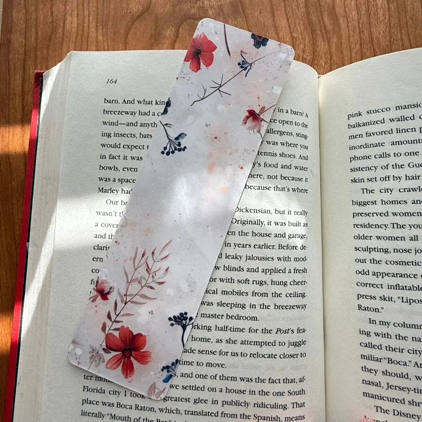 Tan floral bookmark laying on a book on a brown table.