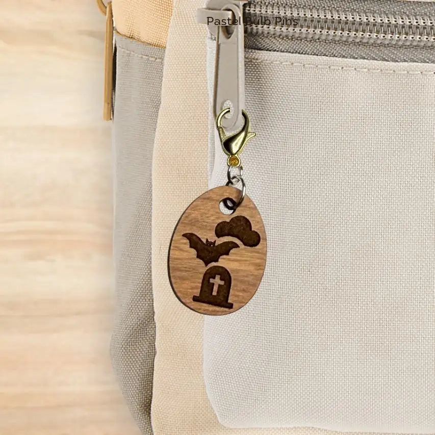 Wooden charm with bat and cross design attached to a beige bag.