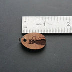Wooden pendant with engraved cat design next to a ruler on a dark surface