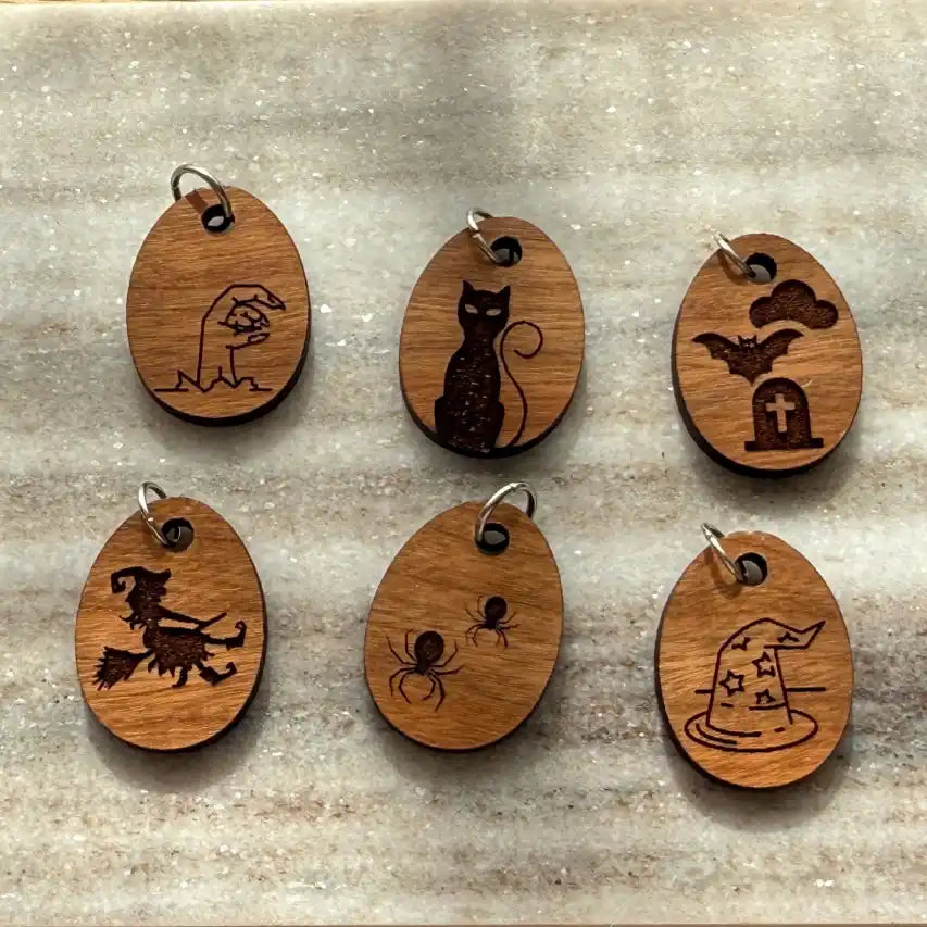 Set of six wooden charms with Halloween-themed designs on a stone surface.