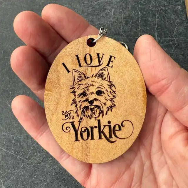 Wooden keychain with 'I Love My Yorkie' engraving held in a hand against a dark background