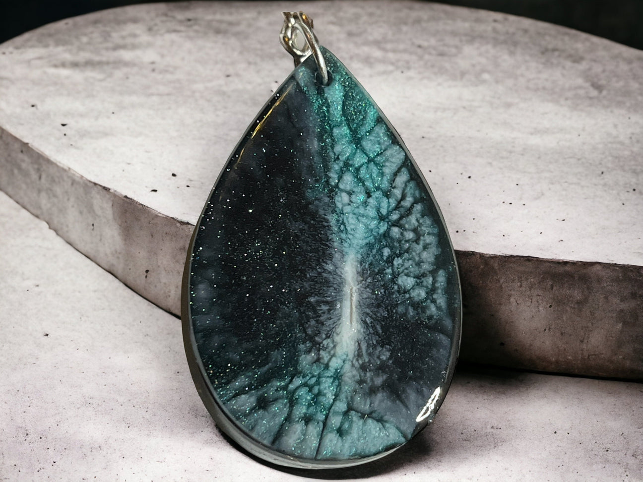 A green resin teardrop-shaped keychain with a silver split ring and lobster clasp, displayed on a textured grey background.