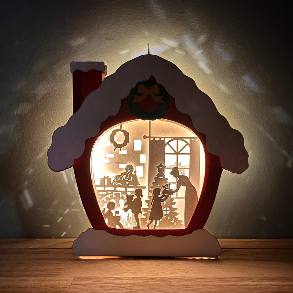 A handcrafted paper cut design Christmas house night light, depicting a festive scene with a Christmas tree and people inside.