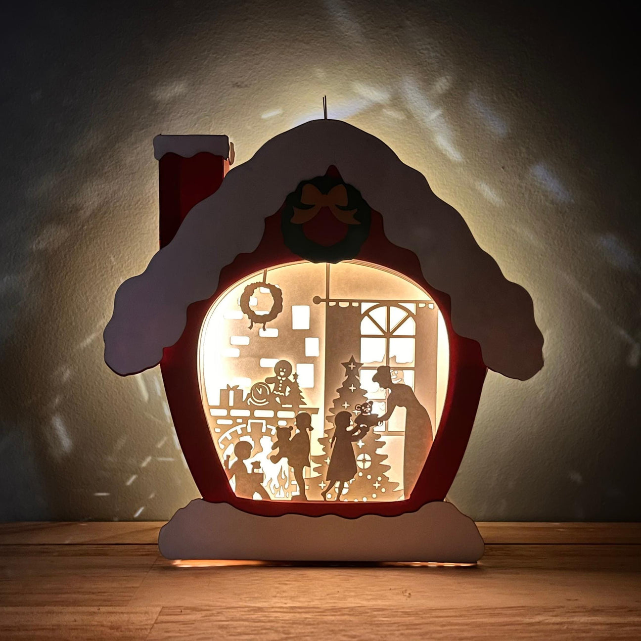 A handcrafted paper cut design Christmas house night light, depicting a festive scene with a Christmas tree and people inside.