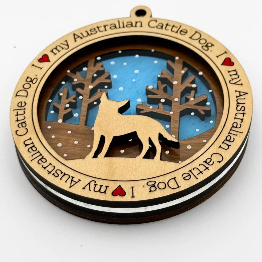 Decorative ornament with an Australian Cattle Dog silhouette against light blue forest scene and engraved text on a white background