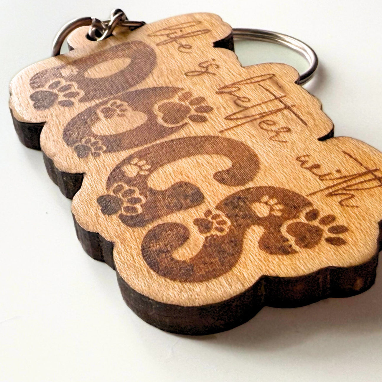 Wooden dog keychain with engraved paw prints and text on a white background