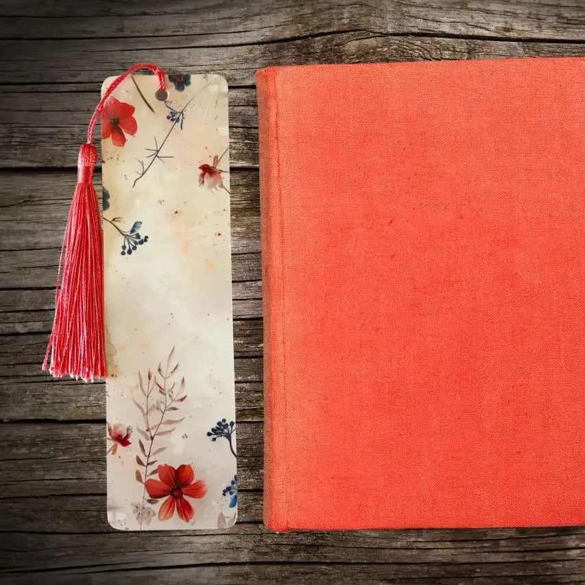 Floral bookmark with a tassel next to a red book on a wooden surface